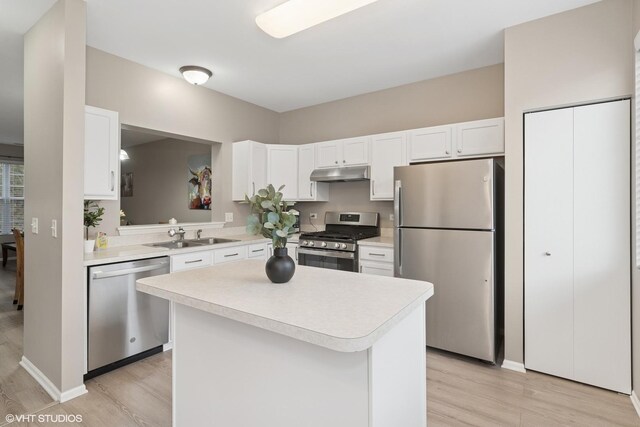 kitchen with light wood-style flooring, stainless steel appliances, light countertops, under cabinet range hood, and a sink