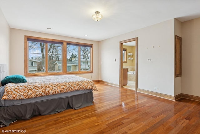 bedroom with connected bathroom, light wood-style flooring, and baseboards