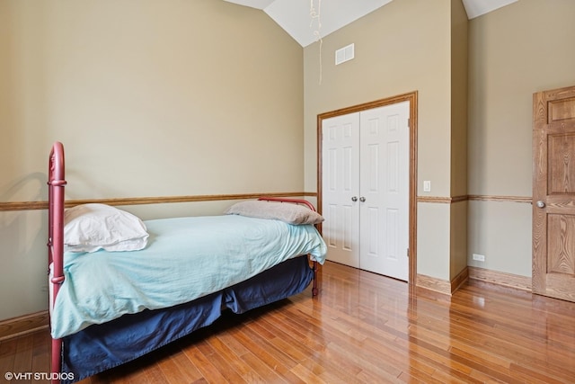 bedroom featuring light wood-type flooring, visible vents, vaulted ceiling, and baseboards