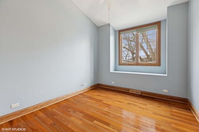 empty room with light wood-style floors, visible vents, vaulted ceiling, and baseboards