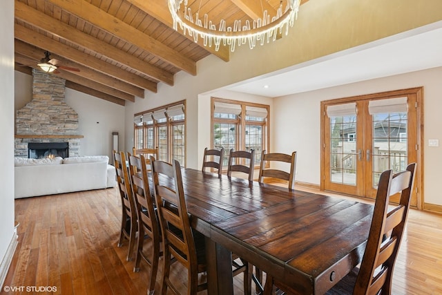 dining space with french doors, vaulted ceiling with beams, wood-type flooring, a stone fireplace, and wooden ceiling