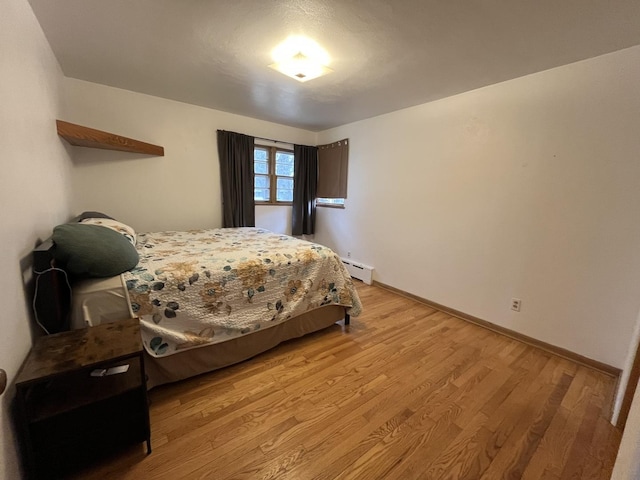 bedroom featuring a baseboard radiator, light wood-style flooring, and baseboards