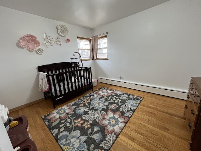 bedroom featuring a baseboard heating unit, wood finished floors, and baseboards