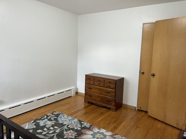 bedroom with a baseboard radiator, baseboards, and wood finished floors