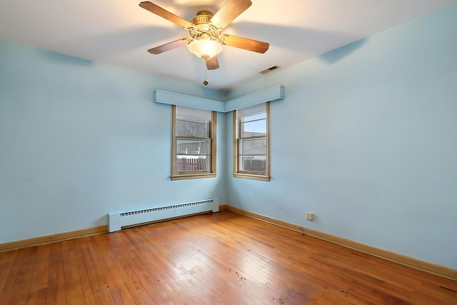 spare room featuring visible vents, a baseboard heating unit, a ceiling fan, baseboards, and hardwood / wood-style flooring