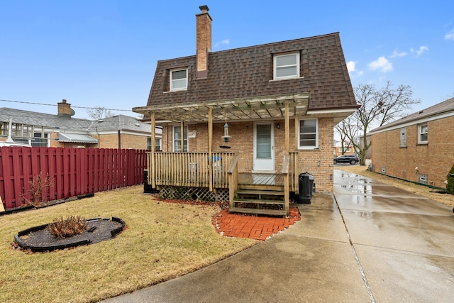 back of house featuring mansard roof, brick siding, fence, a yard, and roof with shingles