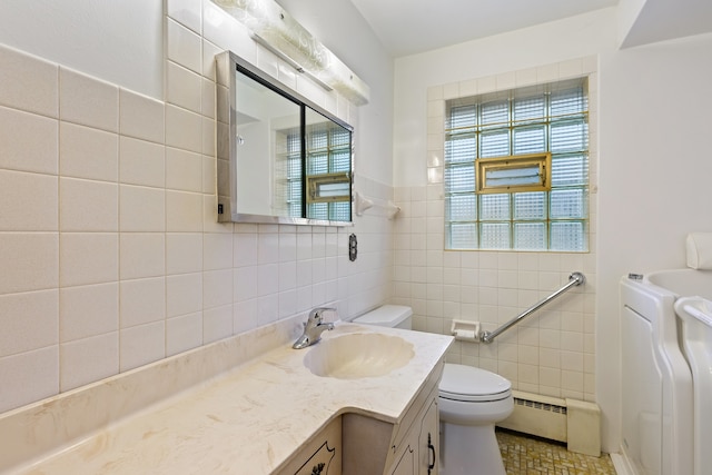 full bathroom featuring tile walls, toilet, baseboard heating, vanity, and washer / dryer