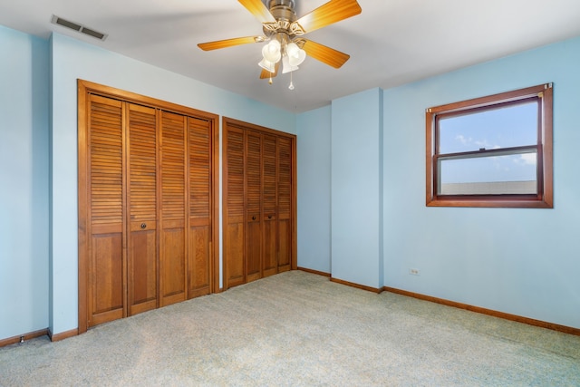 unfurnished bedroom with two closets, light colored carpet, visible vents, ceiling fan, and baseboards