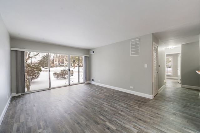 empty room featuring dark wood-style floors, visible vents, and baseboards