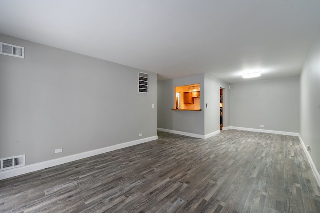 empty room featuring dark wood-type flooring, visible vents, and baseboards