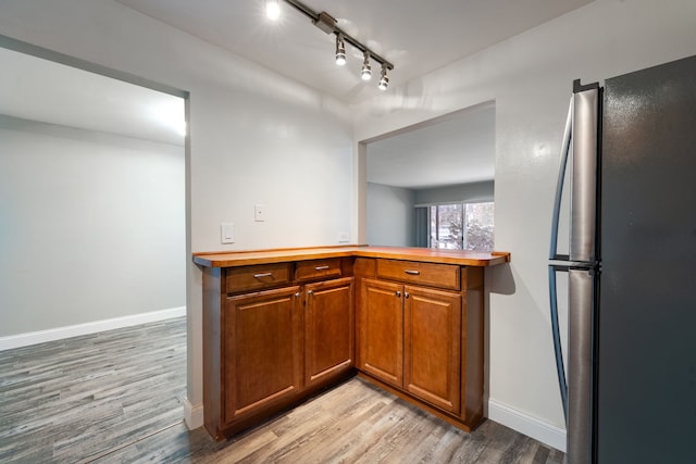 kitchen with baseboards, brown cabinetry, freestanding refrigerator, rail lighting, and light wood-style floors