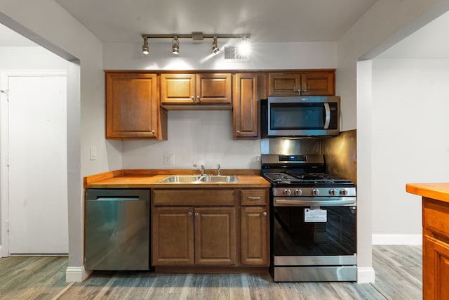 kitchen with baseboards, butcher block countertops, appliances with stainless steel finishes, light wood-style floors, and a sink