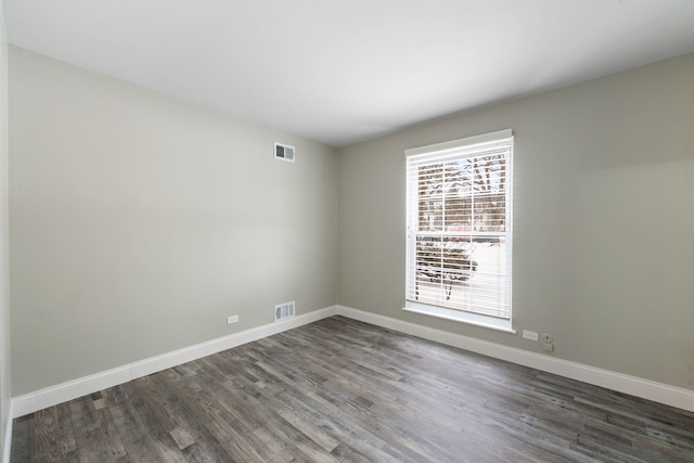 spare room with dark wood-style flooring, visible vents, and baseboards