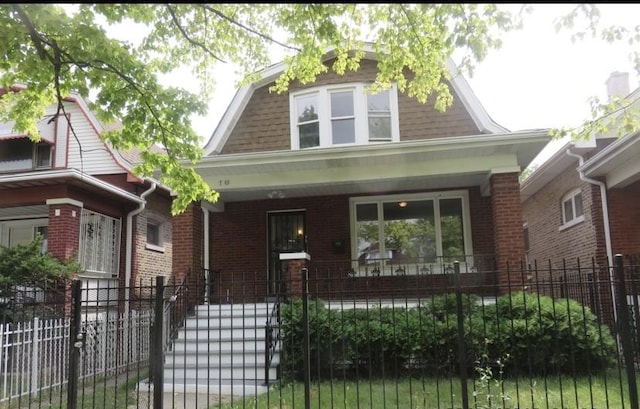 view of front of home featuring a porch, a fenced front yard, brick siding, and a gambrel roof