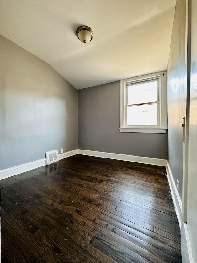 empty room with vaulted ceiling, dark wood-style floors, baseboards, and visible vents