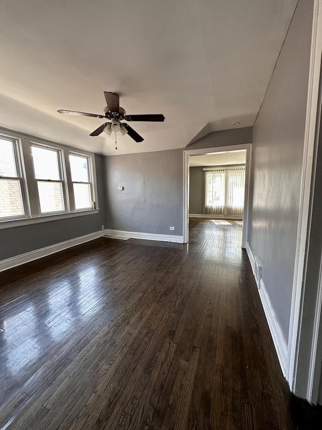 empty room featuring a healthy amount of sunlight, a ceiling fan, dark wood-type flooring, and baseboards