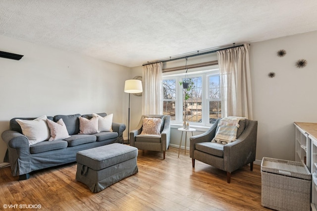 living room with a textured ceiling, light wood-type flooring, and baseboards