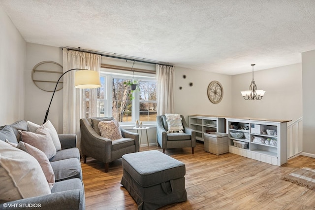 living room featuring a textured ceiling, light wood-type flooring, baseboards, and a notable chandelier