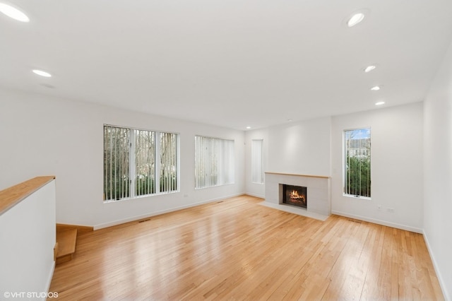 unfurnished living room featuring recessed lighting, baseboards, a fireplace with flush hearth, and light wood-style floors