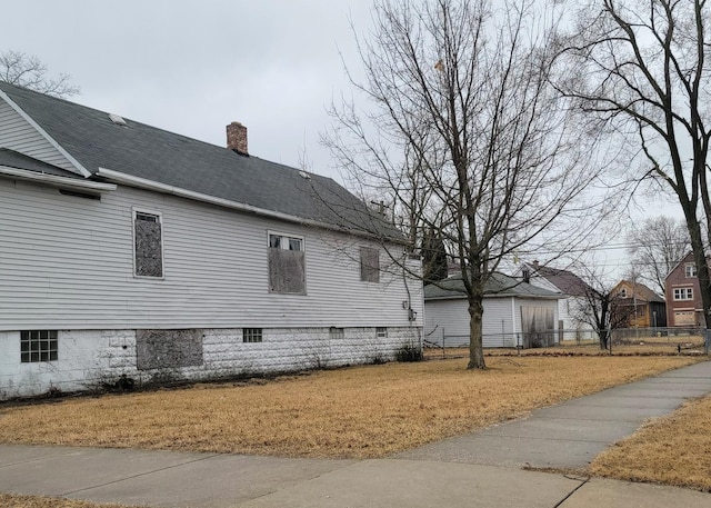 view of side of property with a yard, a shingled roof, a chimney, and fence