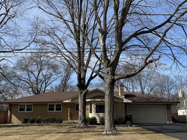 view of front facade featuring fence, an attached garage, a chimney, aphalt driveway, and brick siding