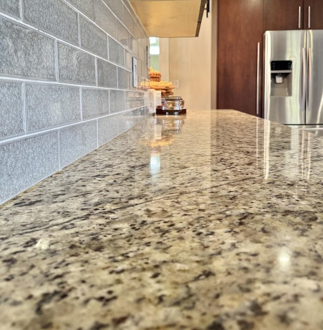 interior details with stainless steel fridge, tasteful backsplash, and light stone countertops