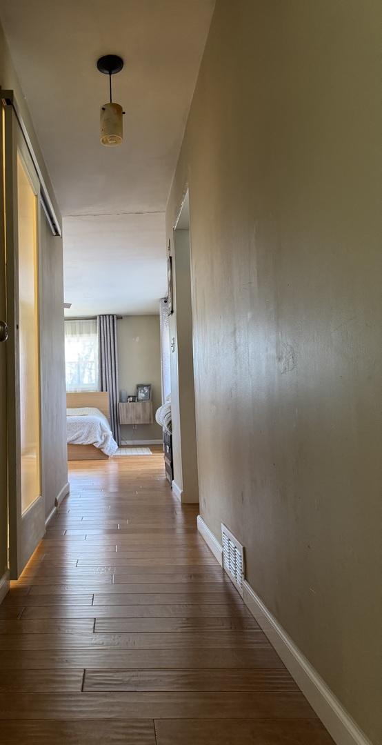 hall featuring visible vents, baseboards, and wood-type flooring