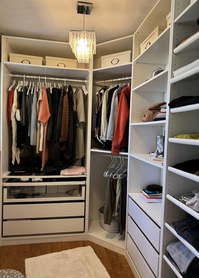 spacious closet with wood finished floors and a chandelier