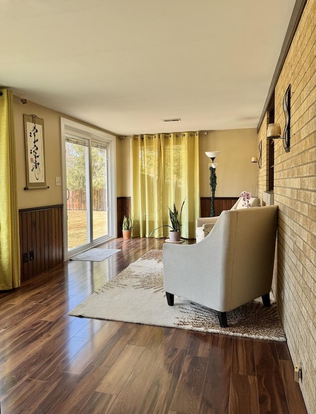 living room with wood finished floors, visible vents, brick wall, and wainscoting