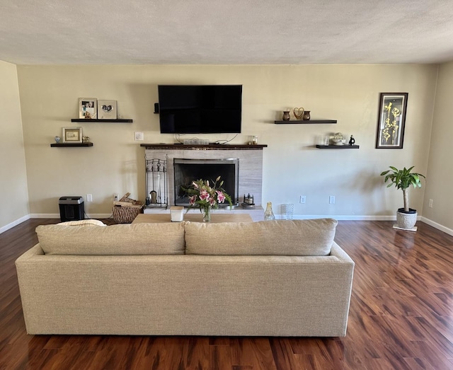 living room with a textured ceiling, dark wood-style floors, baseboards, and a fireplace with raised hearth