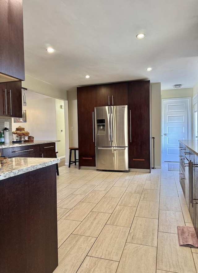 kitchen featuring dark brown cabinets, baseboards, light stone counters, recessed lighting, and stainless steel refrigerator with ice dispenser