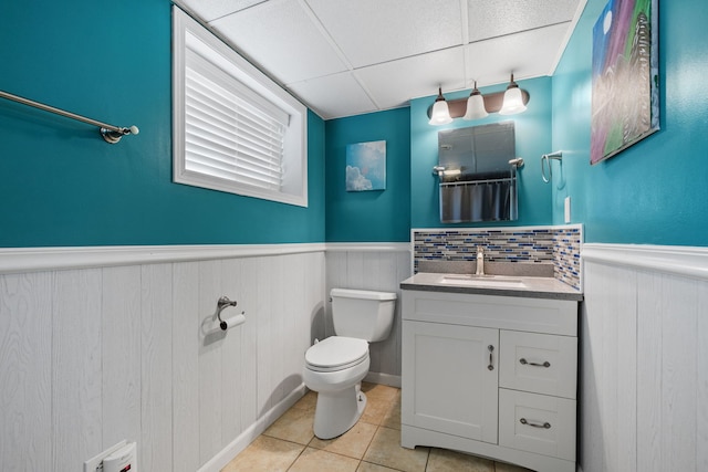 bathroom featuring tile patterned flooring, wainscoting, a drop ceiling, and toilet