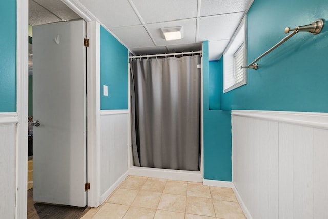 full bathroom with a wainscoted wall, curtained shower, a drop ceiling, and tile patterned flooring