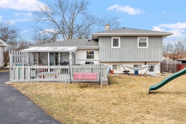 rear view of property with a shingled roof, a lawn, a chimney, fence, and a playground