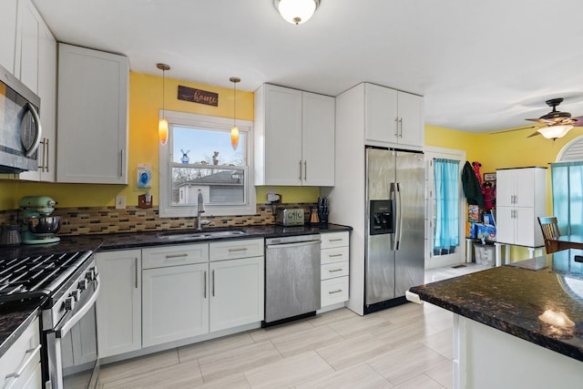 kitchen with a sink, white cabinets, hanging light fixtures, appliances with stainless steel finishes, and dark stone countertops