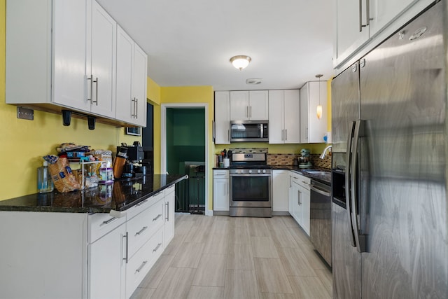 kitchen with stainless steel appliances, white cabinets, a sink, and dark stone countertops