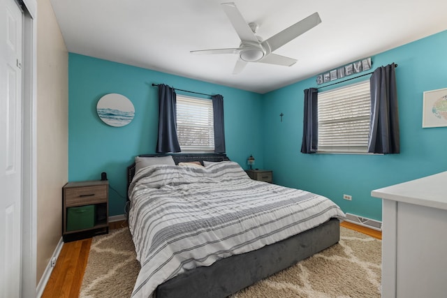 bedroom with a ceiling fan, visible vents, baseboards, and wood finished floors