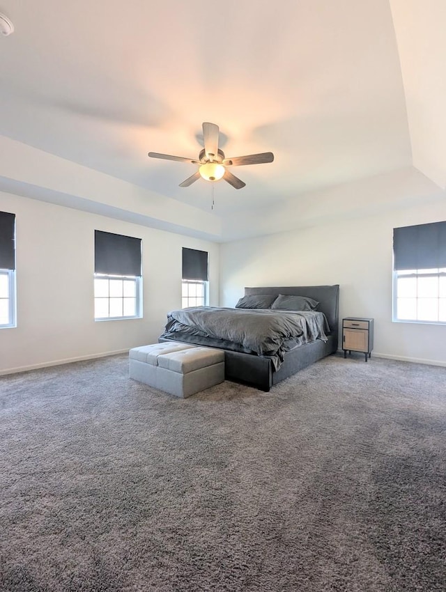 carpeted bedroom featuring baseboards, a raised ceiling, and a ceiling fan