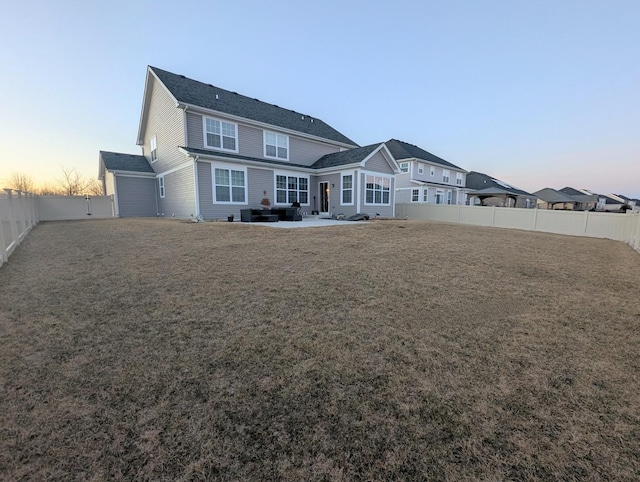 back of property at dusk featuring a lawn, a fenced backyard, and a patio area