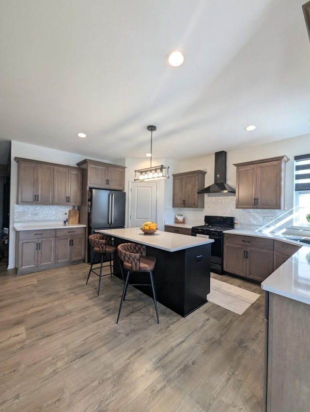 kitchen with a kitchen bar, a center island, black gas stove, wall chimney range hood, and light countertops