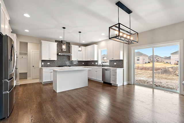 kitchen featuring dark wood-style flooring, white cabinetry, appliances with stainless steel finishes, wall chimney range hood, and decorative backsplash