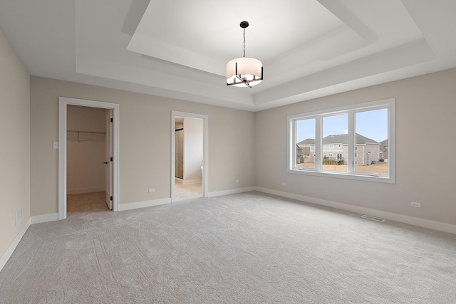 unfurnished bedroom with light carpet, visible vents, baseboards, a raised ceiling, and a walk in closet