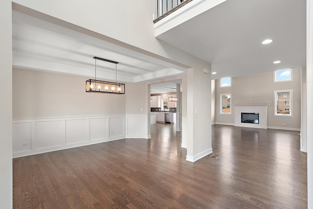 unfurnished living room featuring recessed lighting, a decorative wall, dark wood finished floors, and a glass covered fireplace