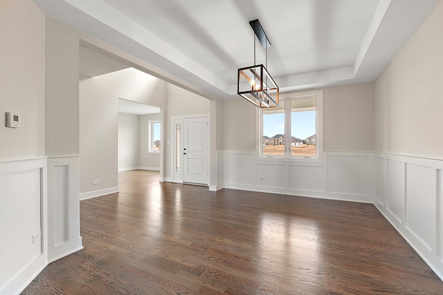 empty room with dark wood-style floors, a raised ceiling, wainscoting, and a chandelier