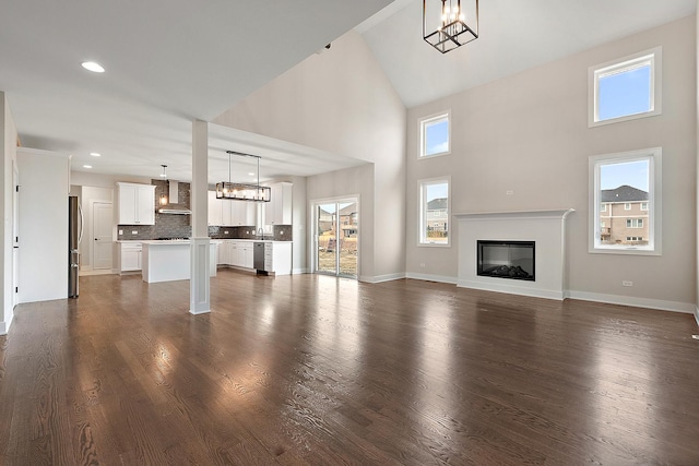 unfurnished living room with baseboards, dark wood finished floors, a glass covered fireplace, a chandelier, and recessed lighting