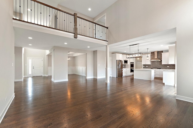 unfurnished living room with recessed lighting, dark wood-style flooring, a high ceiling, and baseboards