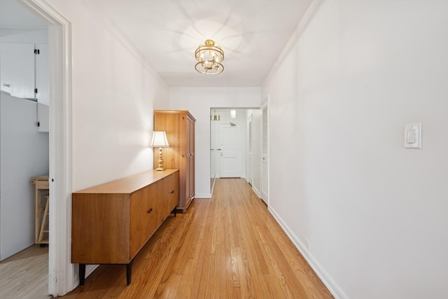 hall with baseboards, light wood-type flooring, and an inviting chandelier