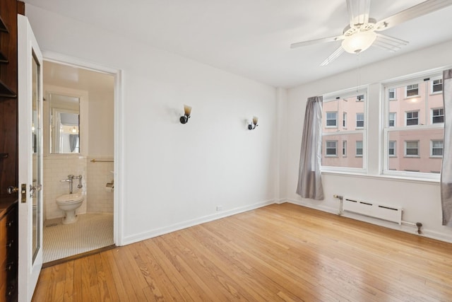 unfurnished room featuring wainscoting, ceiling fan, light wood-style flooring, baseboard heating, and tile walls