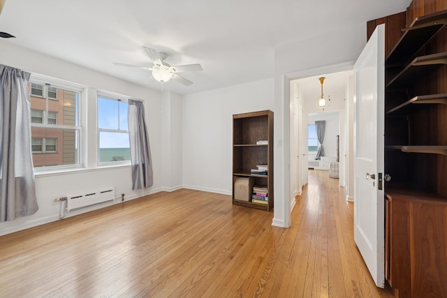 empty room featuring light wood-style floors, a baseboard radiator, baseboards, and a ceiling fan