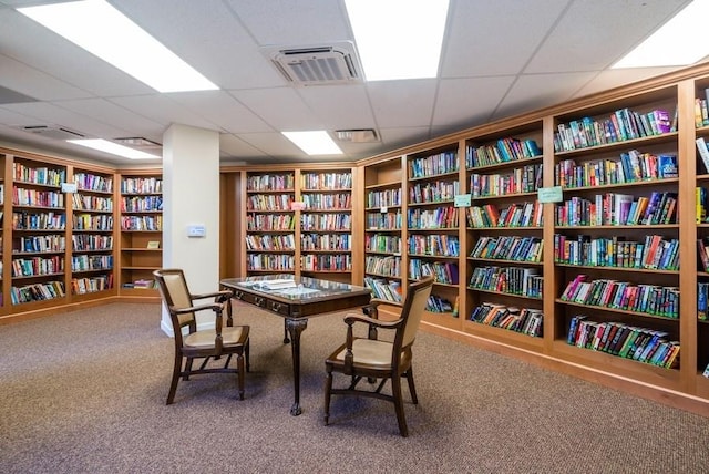 living area with visible vents, wall of books, and carpet flooring